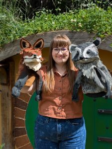 picture of a woman holding up a fox and raccoon puppet.
