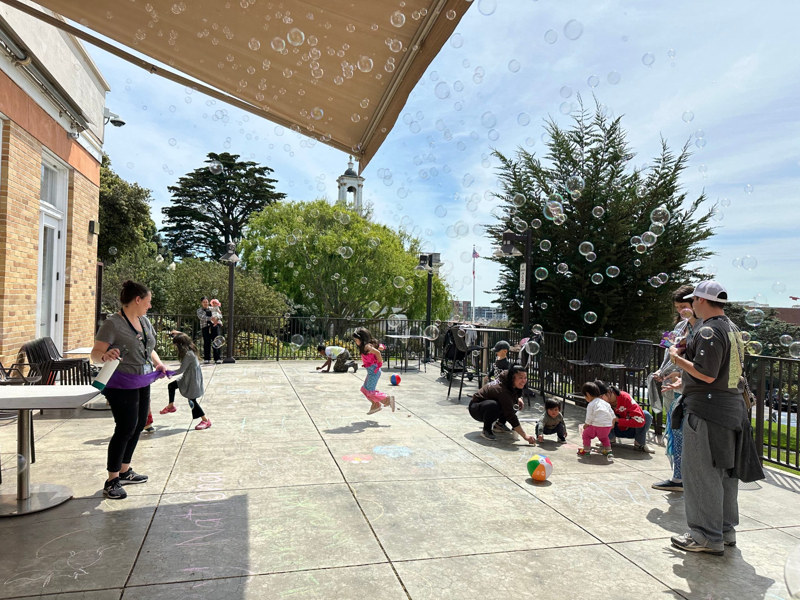 Kids and parents playing on the patio at South San Francisco Library. There are bubbles and chalk drawings on the ground.