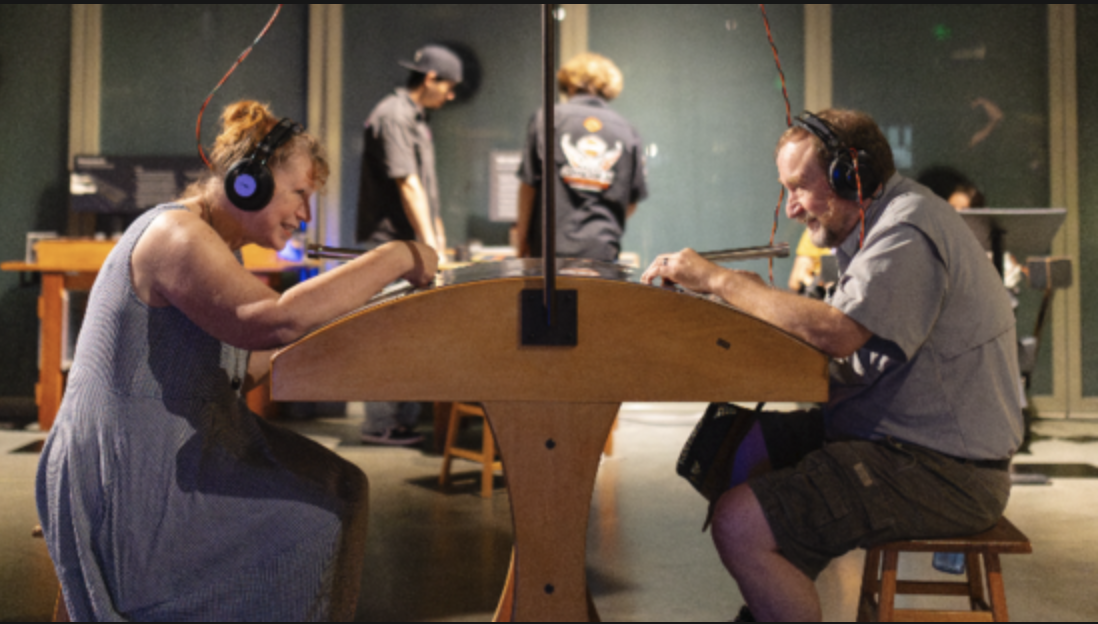 Two adults sitting across from each other smiling, wearing headphones.