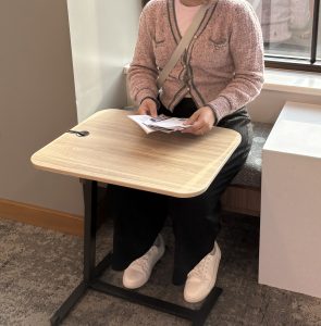 Person sitting on an upholstered bench with a small moveable table.
