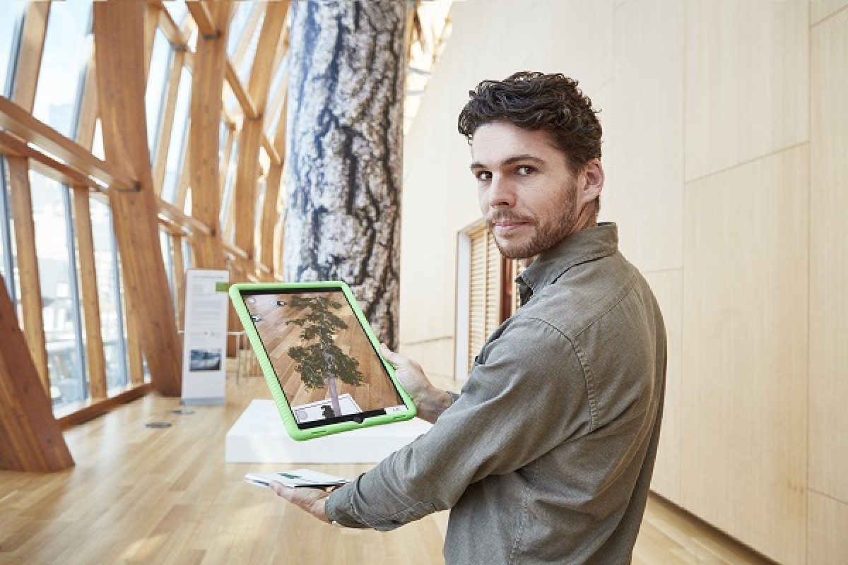 A man stands with a tablet projecting an augmented reality tree in the middle of a gallery