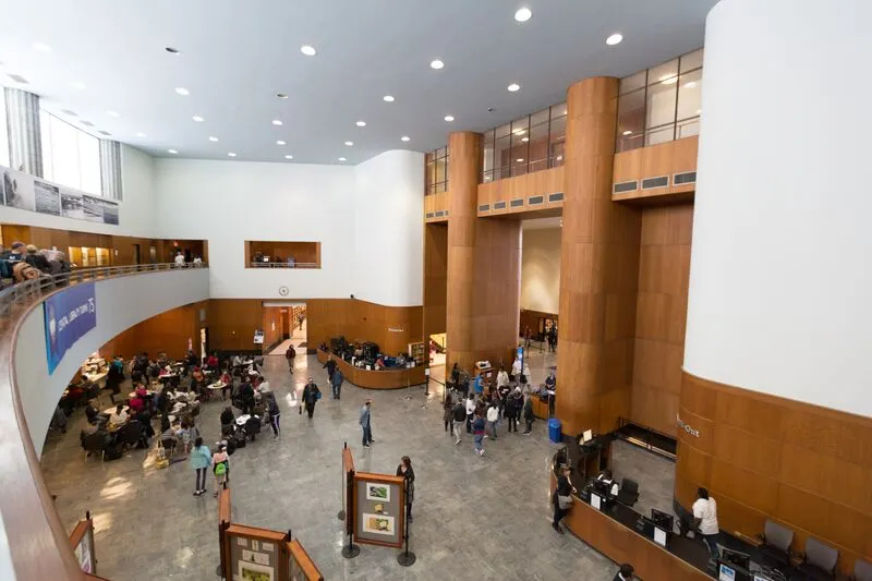 View of the lobby at the Brooklyn Public Library Central branch from the second floor looking down. People are sitting, standing, and walking individually and in groups