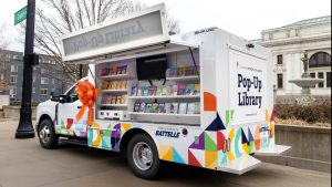A colorful box truck with the side open for access to bookshelves.