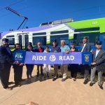 Public transit and library staff holding a sign that says "Read and Ride" in front of a new train.