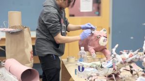 This is a screenshot of a video highlighting the YOUMedia space at the Chicago Public Library. The screenshot includes a person in a gray hoodie and black pants creating a sculpture in the YOUMedia space.