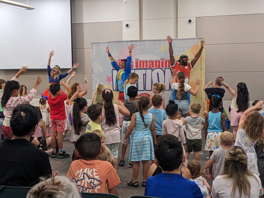 a group of performers in front of a crowd of families at the library