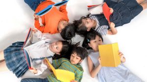 Kids laying down with their heads together in a circle, all reading books.