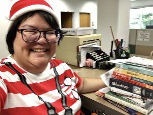 A woman wearing a red and white striped shirt and beanie standing next to a counter with a pile of comic books.
