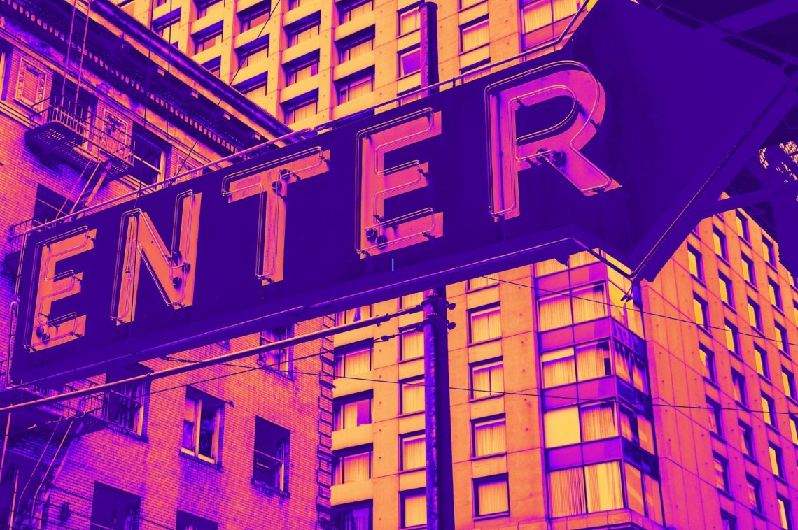a Neon sign with the word “enter” set against a background of high rise buildings.