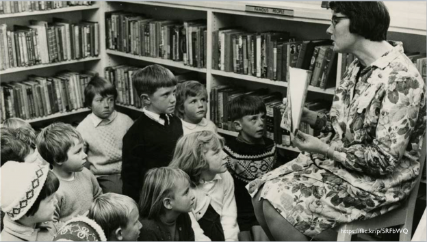 Black and white image of a librarian reading to a group of children in a library